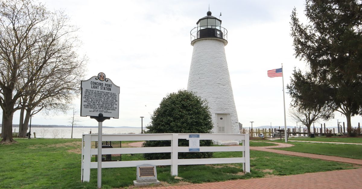 Historic Concord Point Lighthouse standing tall by the water with an American flag in Havre de Grace, Maryland.